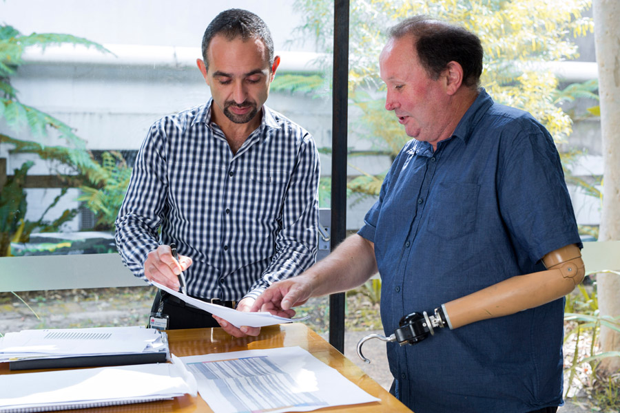 Photo of two males working, one has a prosthetic arm