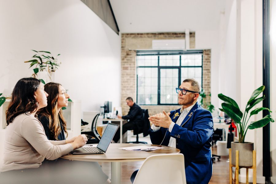 'A person in a blue blazer having a discussion with two other people in an office setting. One is signing Auslan while the others listen.